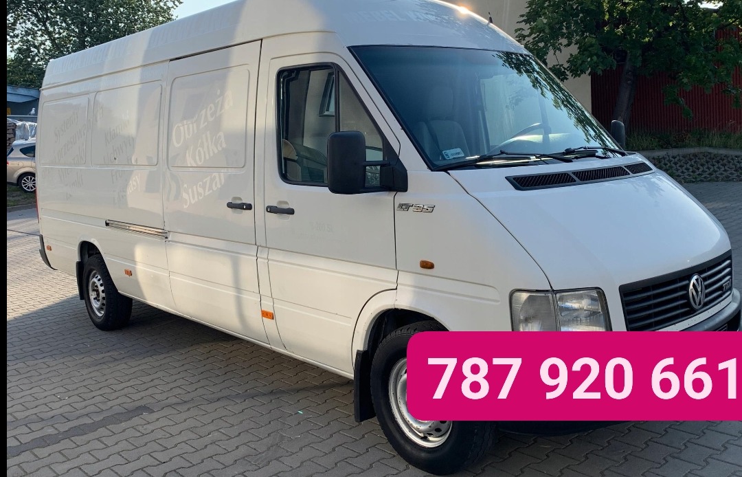 Biały van Volkswagen LT35 z napisem 'Obrzeża Kółka Suszarka' na boku, zaparkowany na kostce brukowej, z numerem telefonu nałożonym na dolną część zdjęcia.