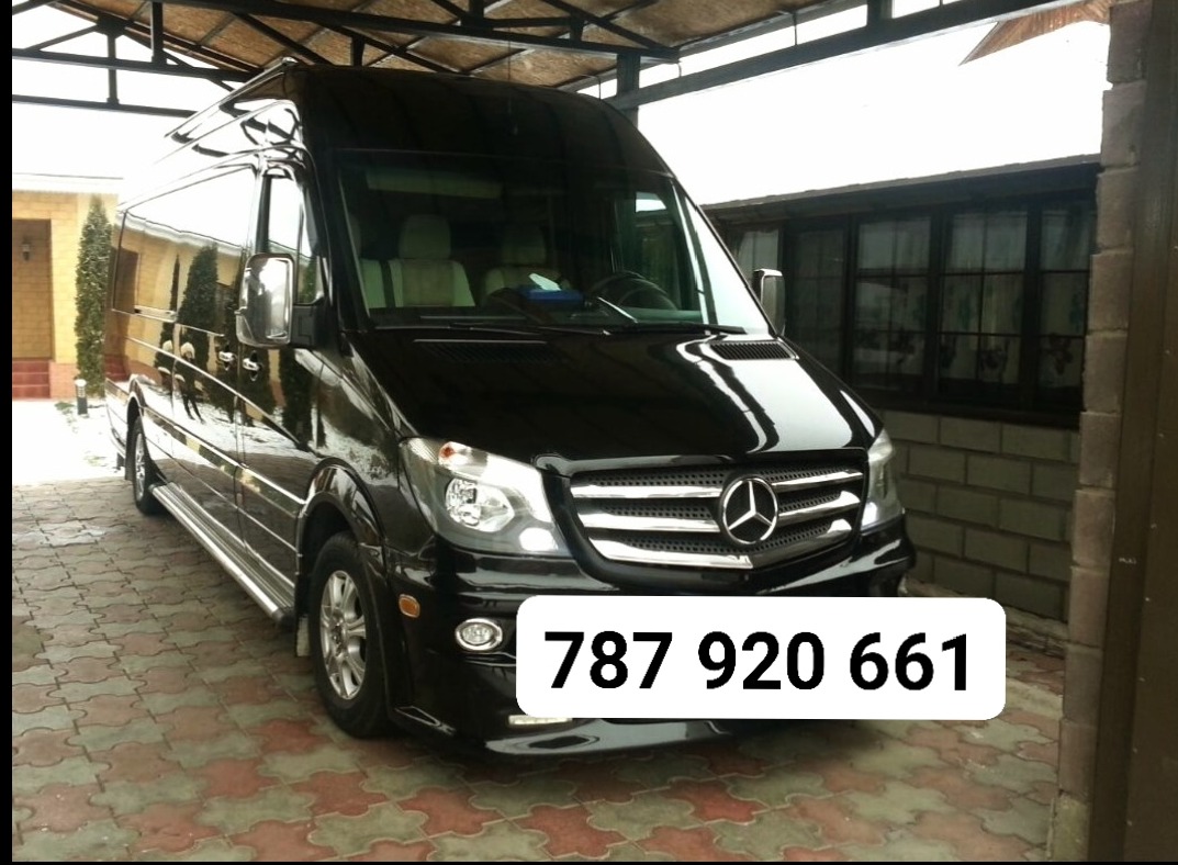 Czarny, lśniący Mercedes-Benz Sprinter, zaparkowany na zewnątrz, z widocznym numerem telefonu nałożonym na zdjęcie. Widoczny fragment budynku w tle.