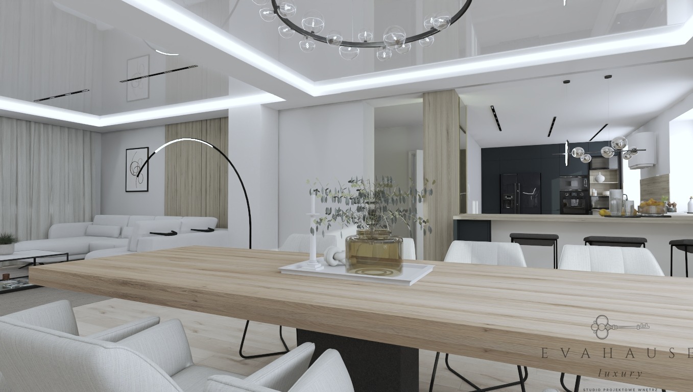Nowoczesne wnętrze: stół z blatem z jasnego drewna, białe krzesła, dekoracje, w tle salon z sofą i kuchnia z czarnymi szafkami. Całość oświetlona designerską lampą.