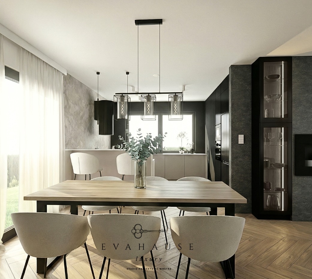 Nowoczesna jadalnia z drewnianym stołem, krzesłami w odcieniach beżu i minimalistycznym oświetleniem. W tle widoczna kuchnia w stonowanych barwach i okno z firanką.