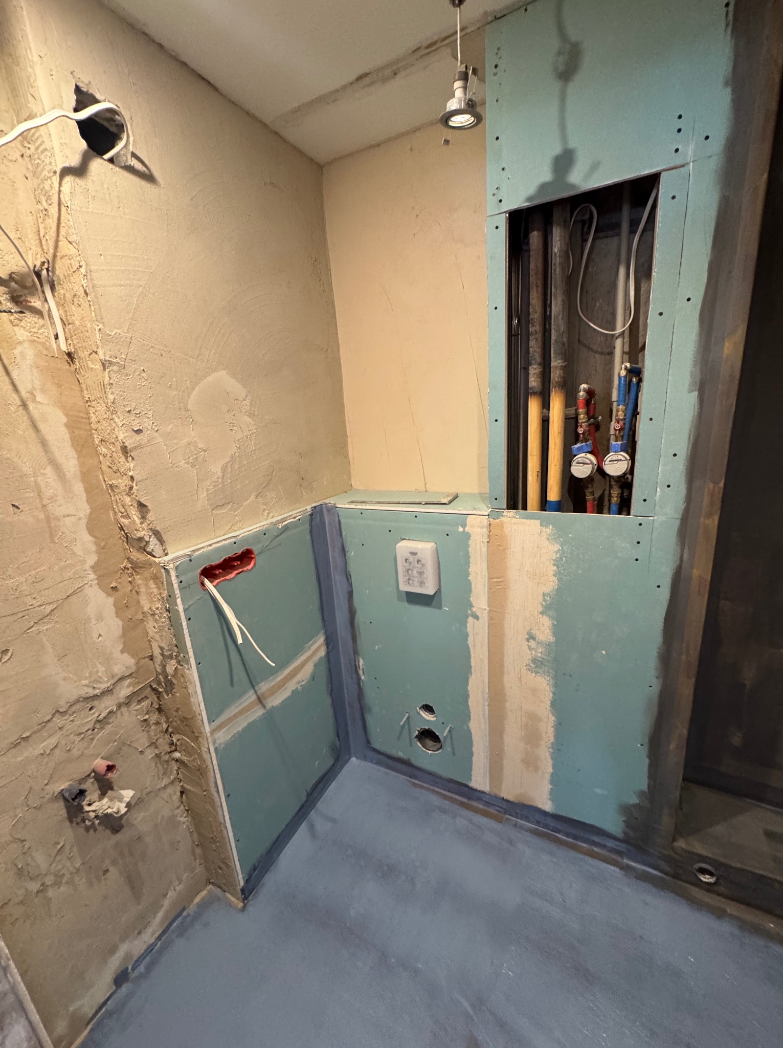 Surowy stan łazienki w trakcie prac: odkryte przewody, niezabezpieczone ściany, instalacja wodna w zabudowie z płyty GK. Widoczne elementy instalacji elektrycznej i wodnej.