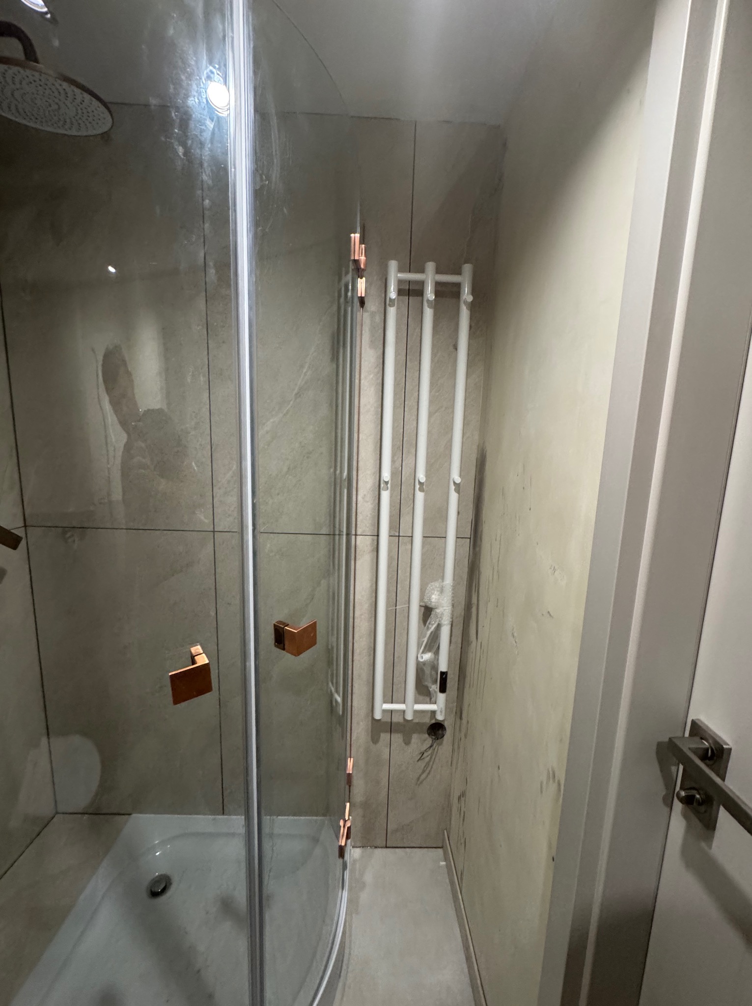 Nowa kabina prysznicowa z grzejnikiem drabinkowym w wykończonej łazience. Widoczne płytki imitujące kamień i detale w kolorze miedzi.