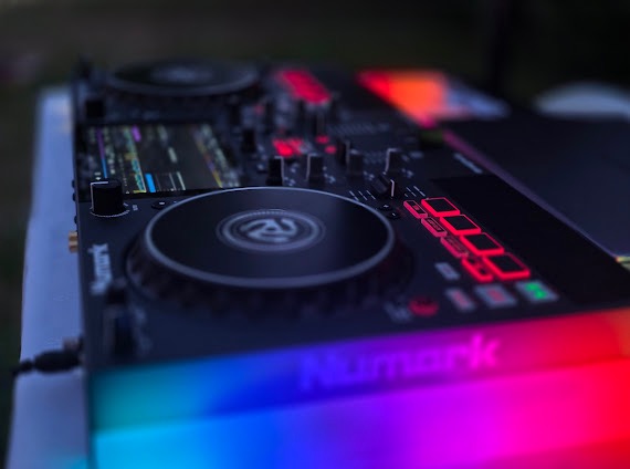 Profesjonalny kontroler DJ Numark z podświetleniem RGB, widoczny w zbliżeniu, na tle zieleni. Sprzęt gotowy do użycia podczas imprezy.