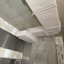 NEXTHOME KOVALEVYCH SPÓŁKA Z OGRANICZONĄ ODPOWIEDZIALNOŚCIĄ - Montaż izolowanych kanałów wentylacyjnych pod surowym stropem. Widoczne płyty kartonowo-gipsowe i surowy beton. Etap prac wykończeniowych w nowym budynku.