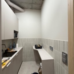 NEXTHOME KOVALEVYCH SPÓŁKA Z OGRANICZONĄ ODPOWIEDZIALNOŚCIĄ - Nowoczesne wnętrze z jasnoszarymi szafkami i blatem. Ściana wykończona pionowymi, ryflowanymi płytkami, powyżej gładka, jasna farba. Surowy betonowy sufit z widoczną instalacją.