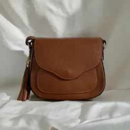 Brązowa torebka z frędzlami na białym tle. Skórzana faktura, delikatne światło, minimalistyczny kadr. Elegancki dodatek, widoczny detal szwu.