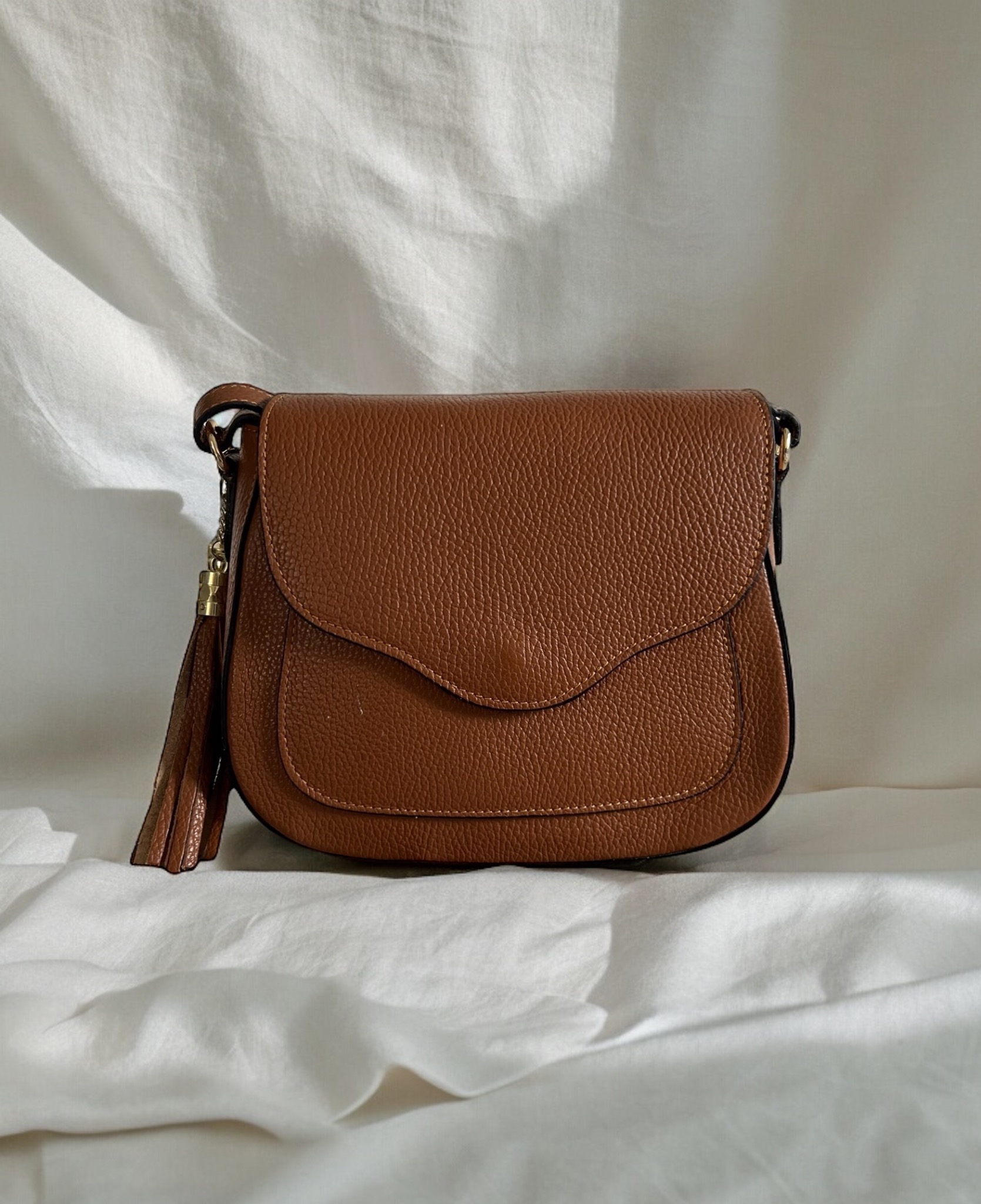 Brązowa torebka z frędzlami na białym tle. Skórzana faktura, delikatne światło, minimalistyczny kadr. Elegancki dodatek, widoczny detal szwu.