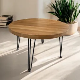 Okrągły stolik kawowy z blatem z jasnego drewna i czarnymi, metalowymi nóżkami typu hairpin, obok doniczka z rośliną i stos książek.