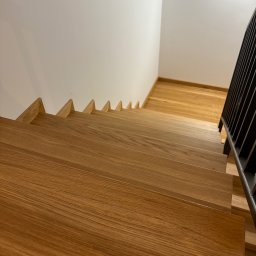 Sklejkovo - Nowoczesne schody z jasnego drewna z czarną balustradą, widok z góry, ukazujący detale słojów drewna i minimalistyczny design.