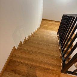 Sklejkovo - Kątowe ujęcie dębowych schodów z czarną, metalową balustradą. Widok z góry na stopnie z naturalnego drewna i minimalistyczne wykończenie.