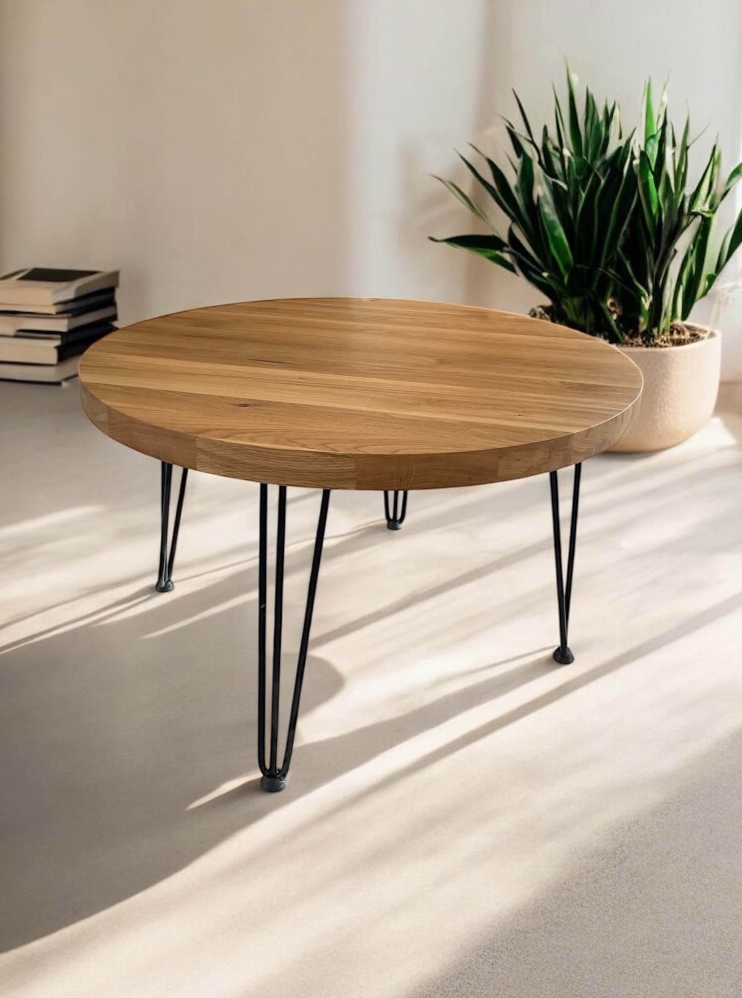 Okrągły stolik kawowy z blatem z jasnego drewna i czarnymi, metalowymi nóżkami typu hairpin, obok doniczka z rośliną i stos książek.