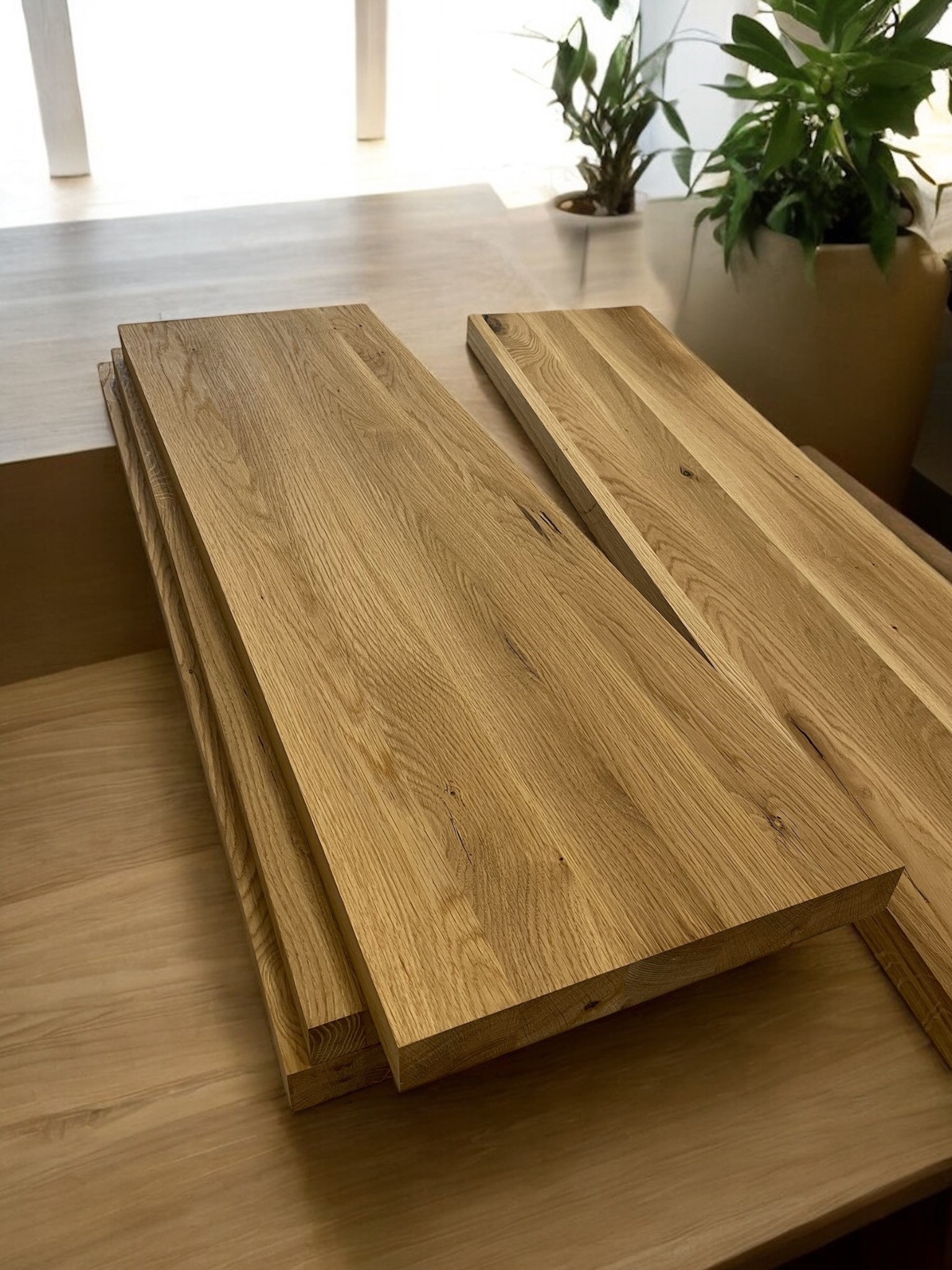 Stos drewnianych blatów/schodów z widocznym usłojeniem, ułożonych na drewnianej powierzchni, z roślinami w tle. Precyzyjne wykonanie stolarskie.