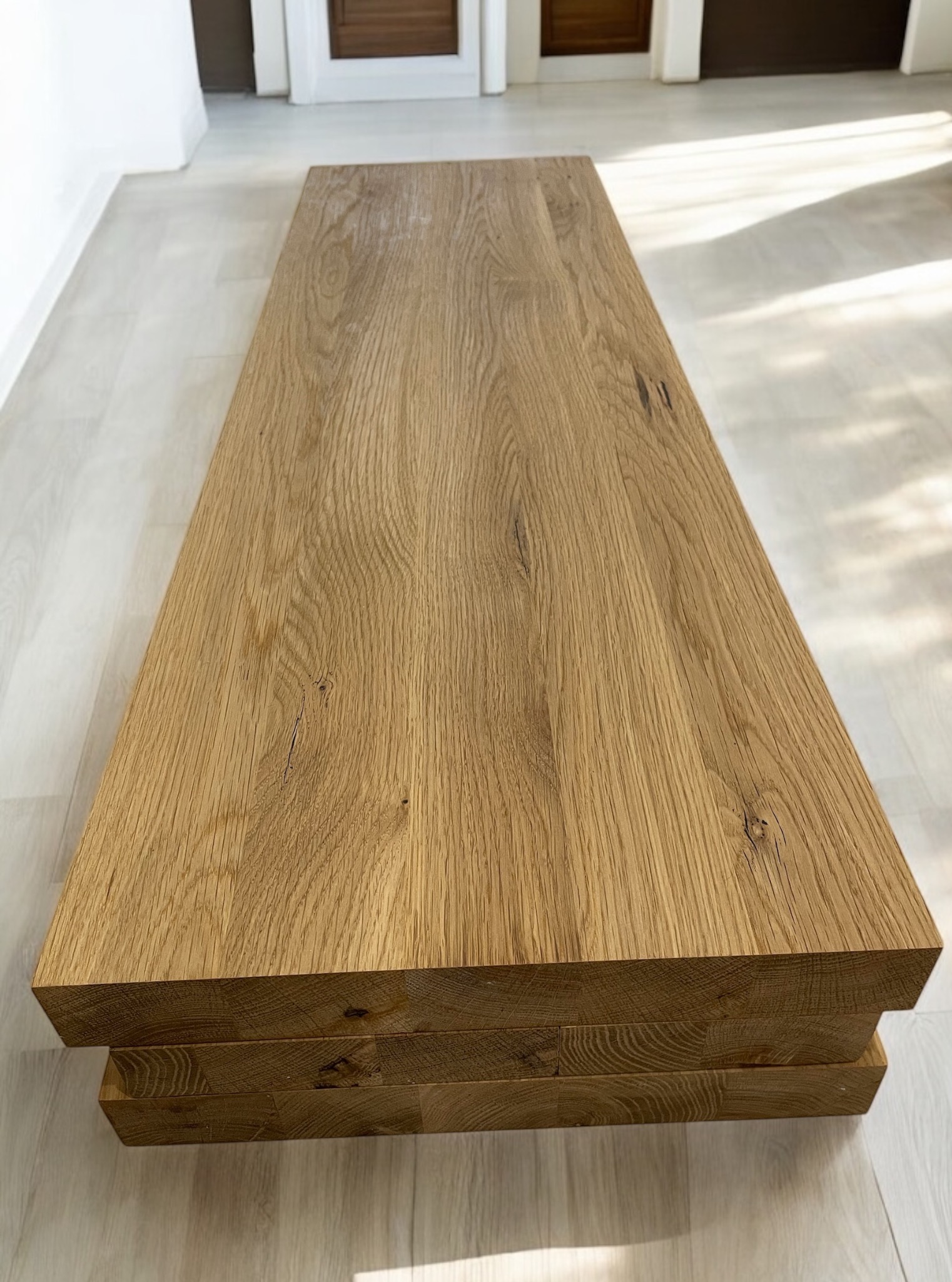 Solidny blat z jasnego drewna dębowego, z widoczną strukturą słojów, ułożony na trzech warstwach drewna, w nowoczesnym wnętrzu z jasną podłogą.