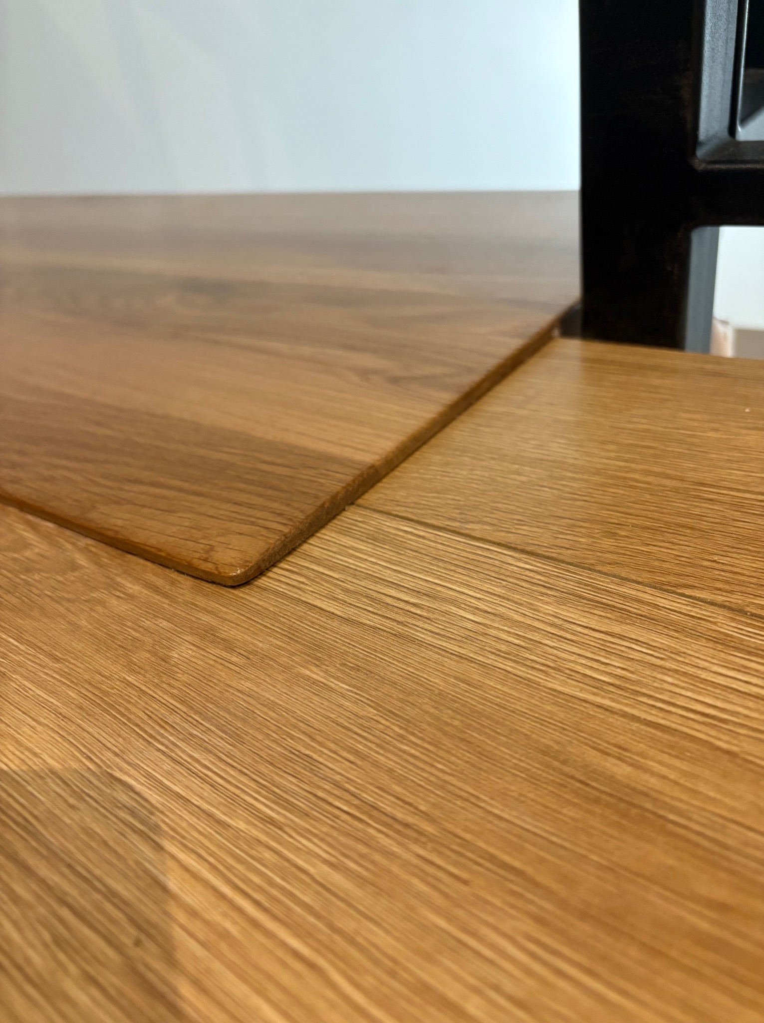 Detale wykończenia blatu z jasnego drewna dębowego, z zaokrąglonym rogiem i widoczną strukturą słojów, fragment czarnej nogi stołu w tle.