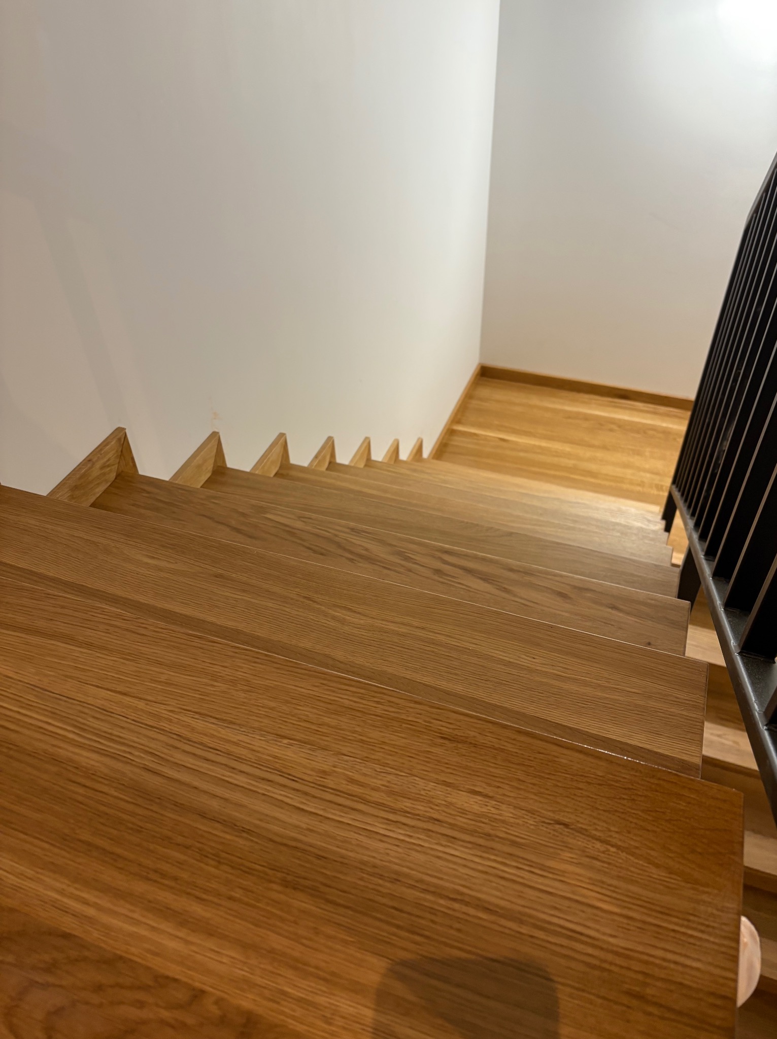 Nowoczesne schody z jasnego drewna z czarną balustradą, widok z góry, ukazujący detale słojów drewna i minimalistyczny design.