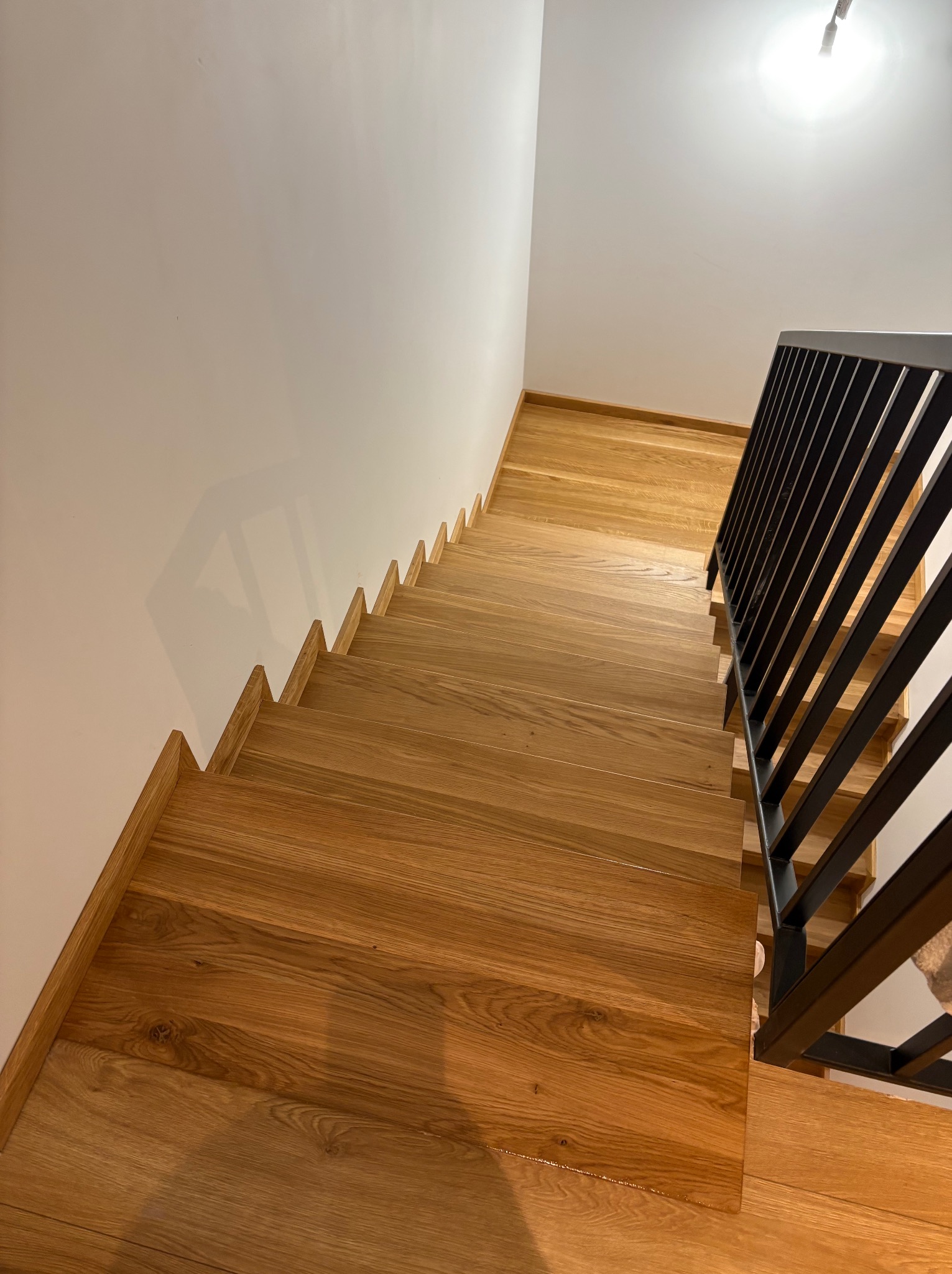 Kątowe ujęcie dębowych schodów z czarną, metalową balustradą. Widok z góry na stopnie z naturalnego drewna i minimalistyczne wykończenie.