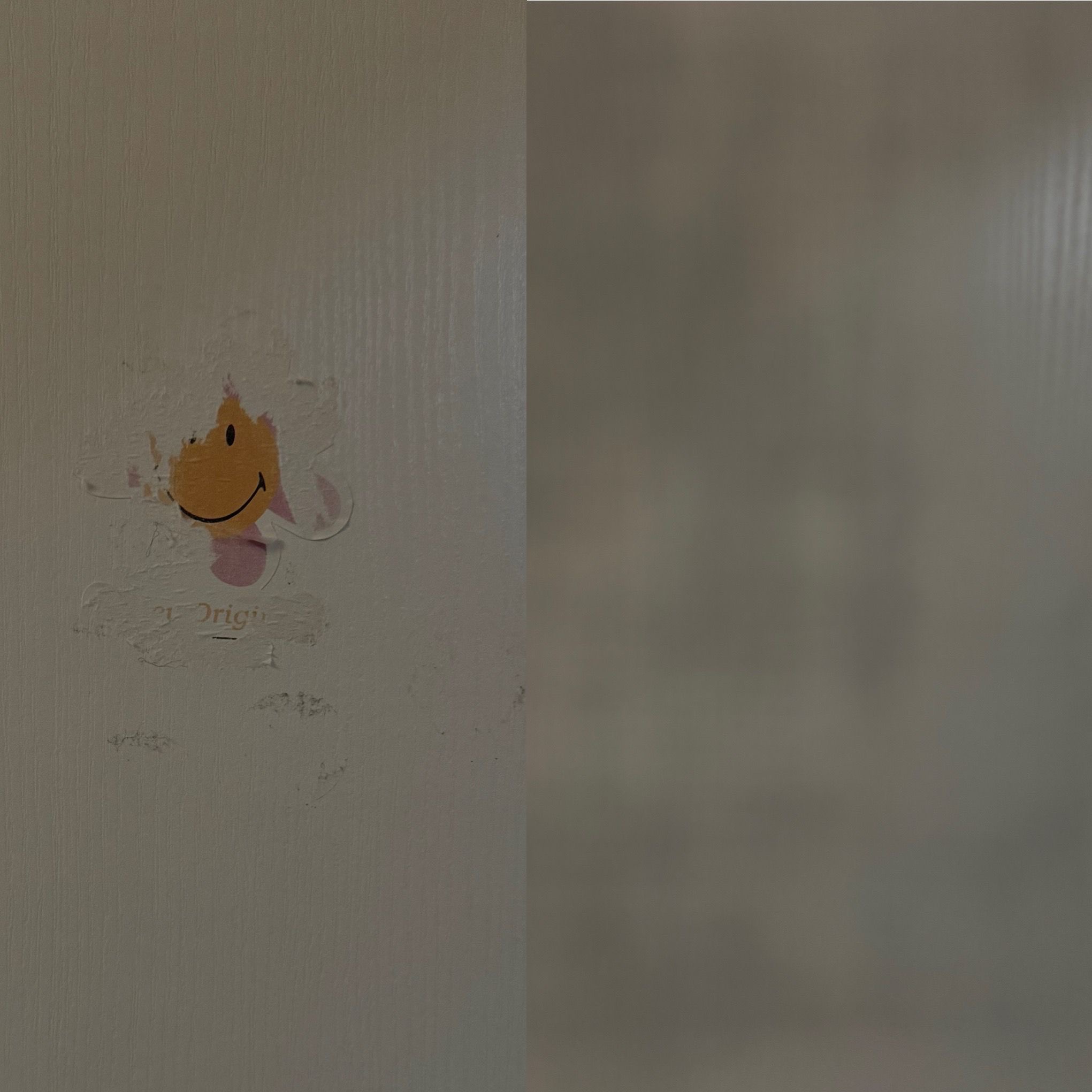 Ściana z resztkami naklejki w kształcie uśmiechniętej buźki, widoczne ślady kleju i zabrudzenia. Po prawej stronie czysta ściana.