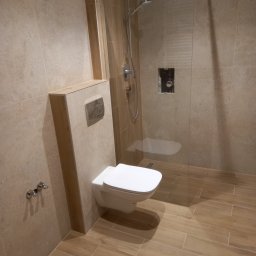 Zakład Instalacyjno-sanitarny INSTAL-MONT Krzysztof Sworski - Nowoczesna łazienka z beżowymi płytkami imitującymi drewno, podwieszana toaleta z chromowanym przyciskiem i kabina prysznicowa typu walk-in z odpływem liniowym.