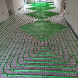 Zakład Instalacyjno-sanitarny INSTAL-MONT Krzysztof Sworski - Zielone rury ogrzewania podłogowego, ułożone w pętle na czerwonej siatce, w trakcie montażu w Nakle nad Notecią. Widok z góry na surową podłogę.