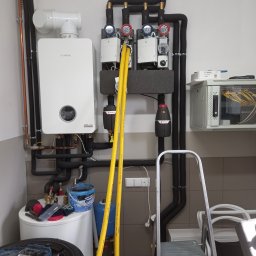 Zakład Instalacyjno-sanitarny INSTAL-MONT Krzysztof Sworski - Nowoczesny piec gazowy Bosch z podłączeniami, widoczne rury w izolacji, manometry i elementy instalacji. Na podłodze narzędzia i akcesoria hydrauliczne.