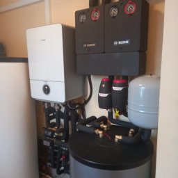 Zakład Instalacyjno-sanitarny INSTAL-MONT Krzysztof Sworski - Złożona instalacja grzewcza Bosch z piecem, zasobnikiem i osprzętem, widoczna w pomieszczeniu technicznym. Rury i zawory tworzą skomplikowany system połączeń.