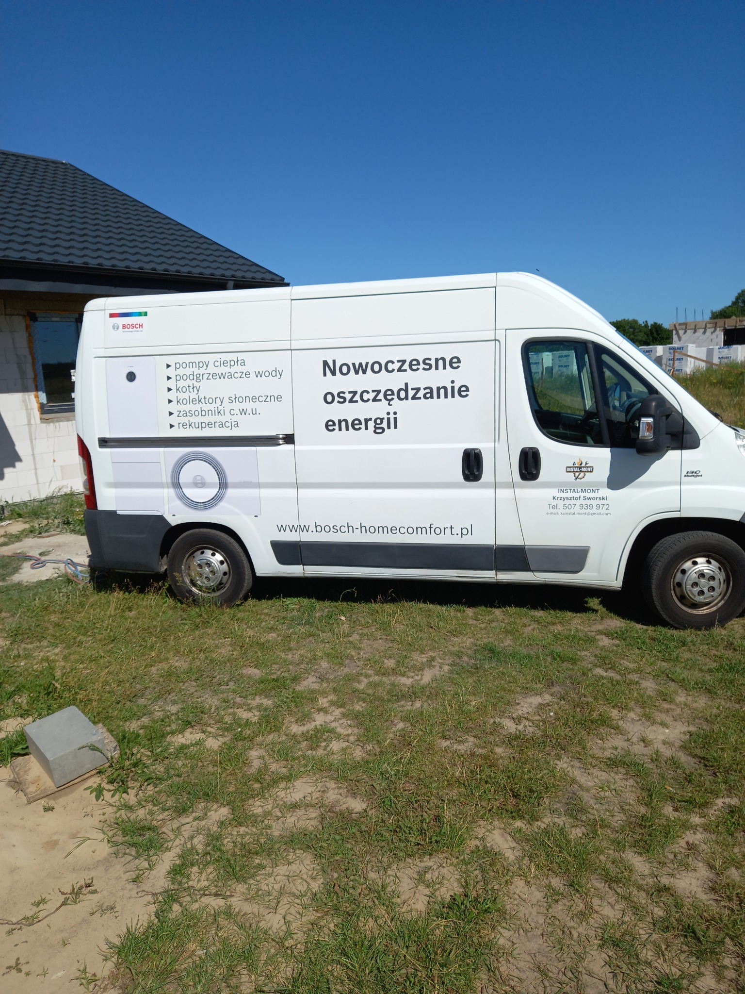 Biały furgon marki Bosch z napisem 'Nowoczesne oszczędzanie energii' na tle budowy domu w stanie surowym, prezentujący usługi instalacyjne. Logo firmy widoczne na pojeździe.