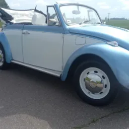 Błękitno-biały, odrestaurowany Volkswagen Garbus Cabrio na asfaltowej drodze w słoneczny dzień. Klasyczny model z otwartym dachem i polerowanymi felgami.