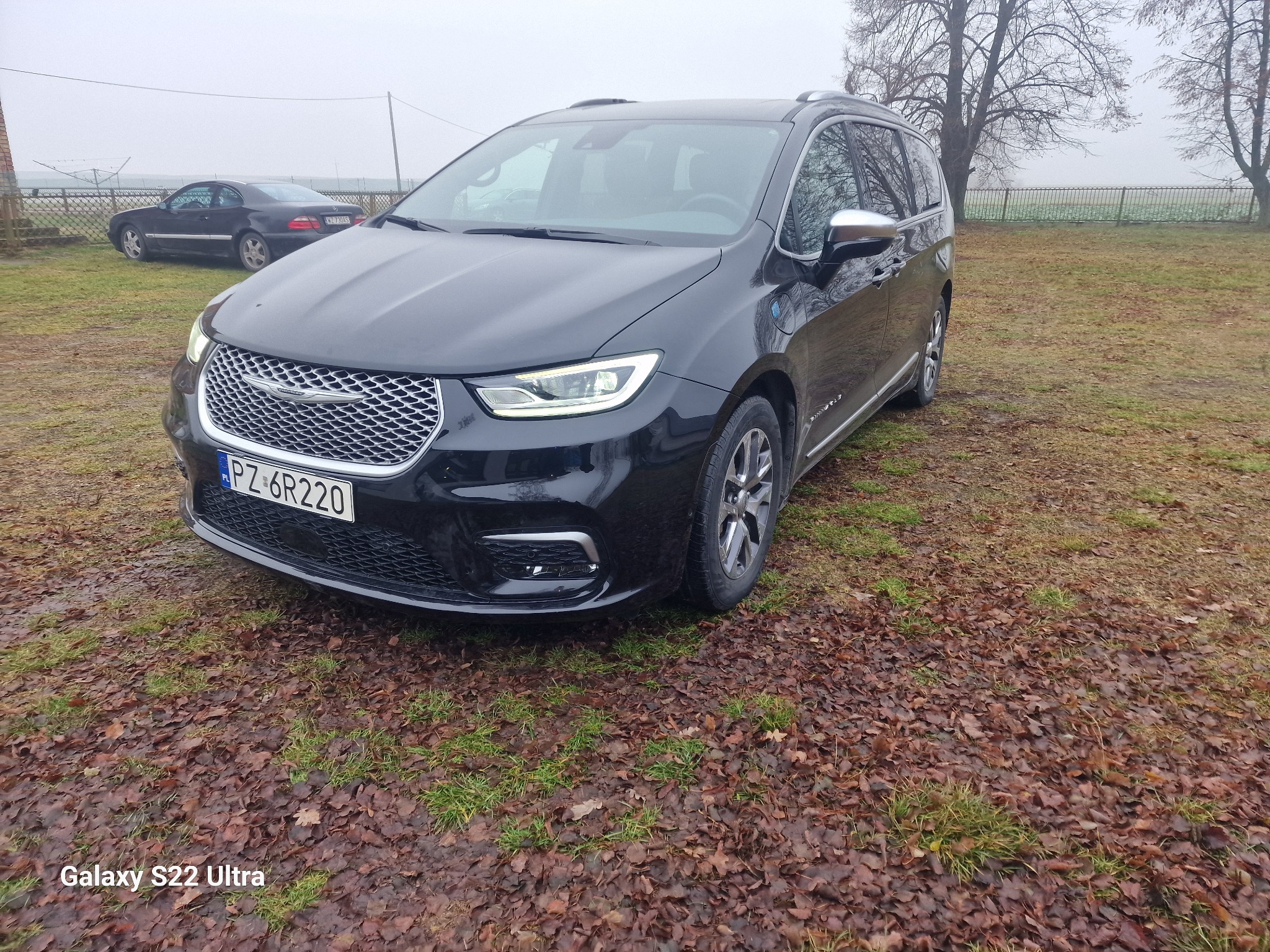 Czarny minivan Chrysler Pacifica z polską tablicą rejestracyjną PZ 6R220, sfotografowany na zewnątrz w pochmurny dzień, z widocznym innym samochodem w tle.