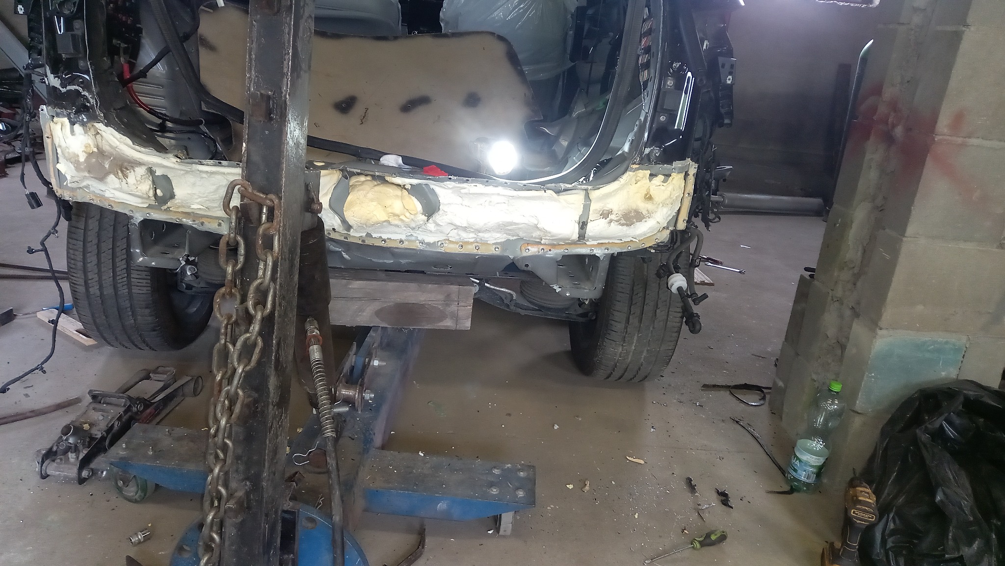 Uszkodzony tył pojazdu na podnośniku warsztatowym, widoczne elementy karoserii w trakcie naprawy, narzędzia i akcesoria blacharskie. Detal warsztatu.