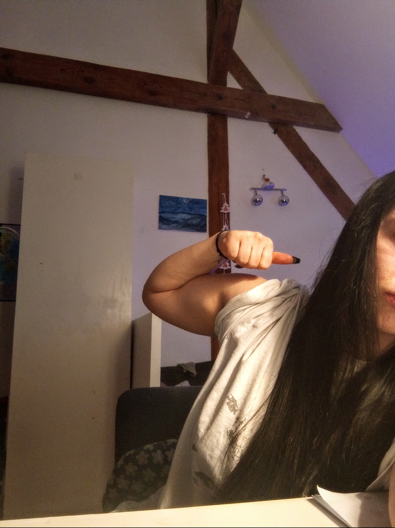 Dziewczyna prezentuje napięty biceps, wskazując na niego palcem. W tle widoczne elementy wystroju wnętrza: drewniane belki stropowe i dekoracje ścienne.