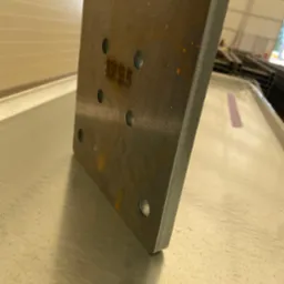 Metalowa płyta z otworami, obróbka skrawaniem, szlifowane krawędzie. Precyzyjne wykonanie w Czastary. Widoczne oznaczenia na powierzchni.