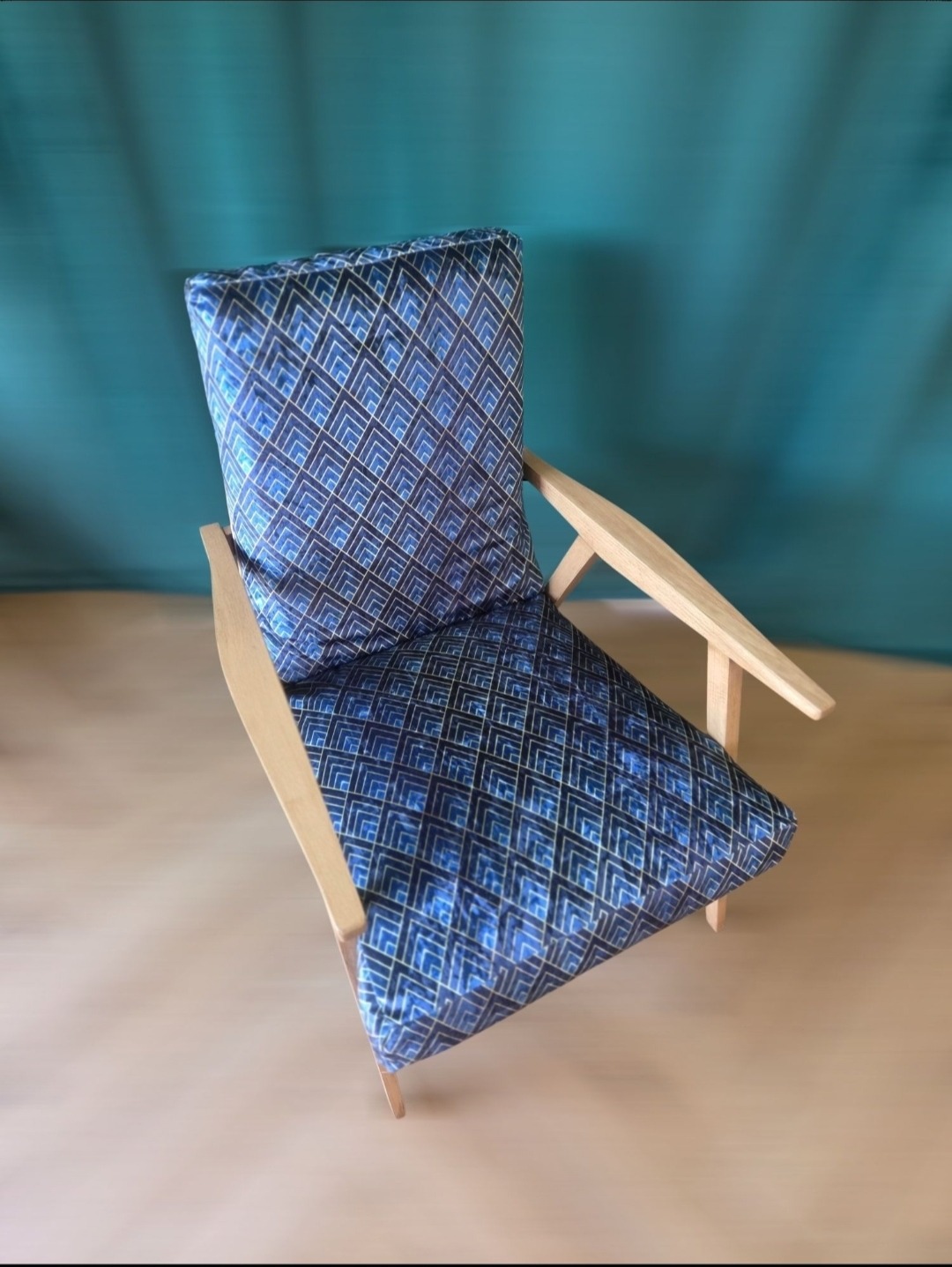 Stylowe krzesło z drewnianą ramą i miękkim siedziskiem w geometryczny wzór na tle turkusowej ściany. Nowoczesny design z akcentem vintage.