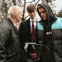 Amper Art Media Production - Adam Perzyna - Ekipa filmowa w plenerze: trzech mężczyzn z kamerą Sony na statywie, monitor podglądowy. Jeden w garniturze z czerwoną koszulą, drugi w bluzie z kapturem, trzeci w kurtce.
