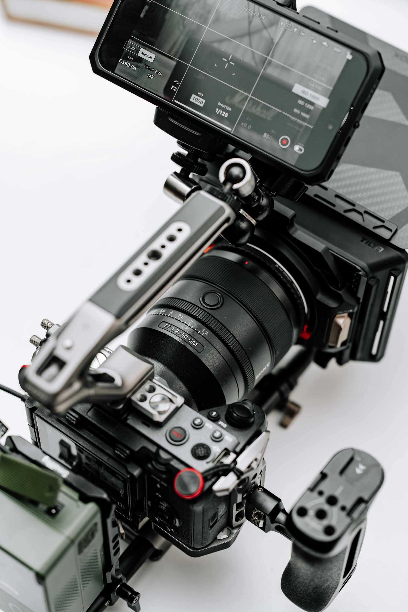 Profesjonalna kamera Sony z obiektywem 50mm, zamontowana na riggu z uchwytami i monitorem podglądowym, ustawiona na białym tle. Widoczne ustawienia ostrości.