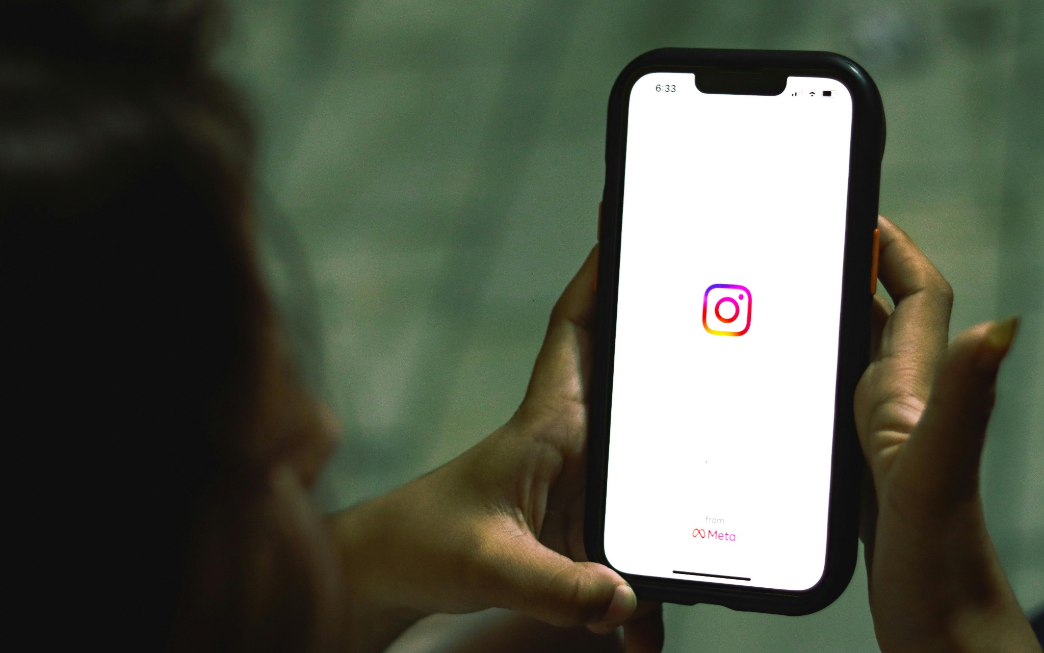 Osoba trzyma smartfon z otwartą aplikacją Instagram, widoczne logo i napis 'from Meta'. Ekran jasny, kontrastuje z ciemnym otoczeniem i kolorem obudowy telefonu.