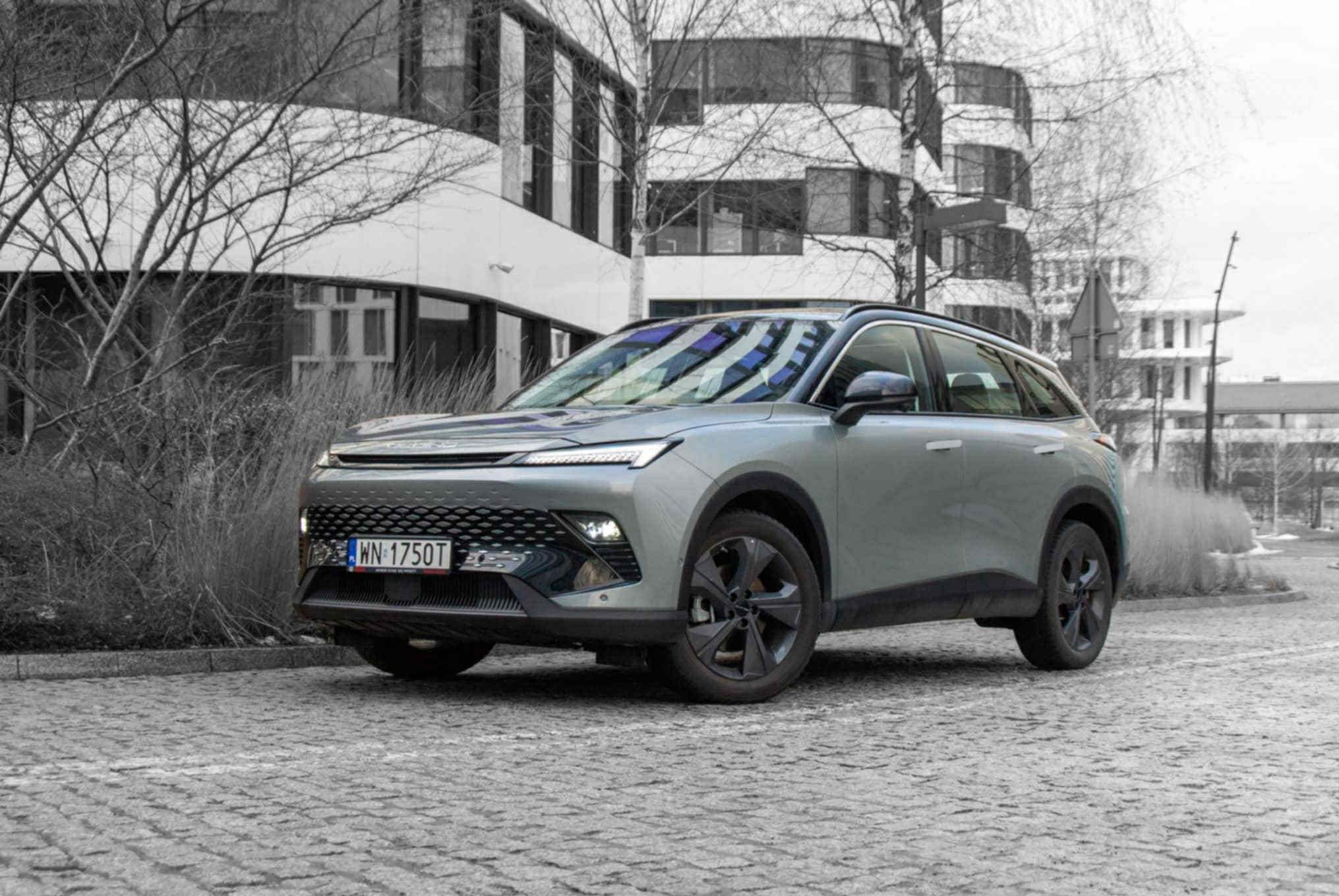 Szary crossover na tle nowoczesnego budynku. Auto z czarnymi felgami i reflektorami LED, zaparkowane na brukowanej nawierzchni. Tablica rejestracyjna WN 1750T.