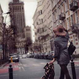 Paulina Dębska photography - Kobieta w kapeluszu i płaszczu na tle miejskiej ulicy z Pałacem Kultury. Ujęcie od tyłu, styl miejski, jesienna kolorystyka, światło naturalne.