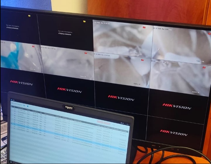 Monitor z podglądem z kamer Hikvision i laptop z konfiguracją systemu monitoringu. Widok zza ramienia instalatora.