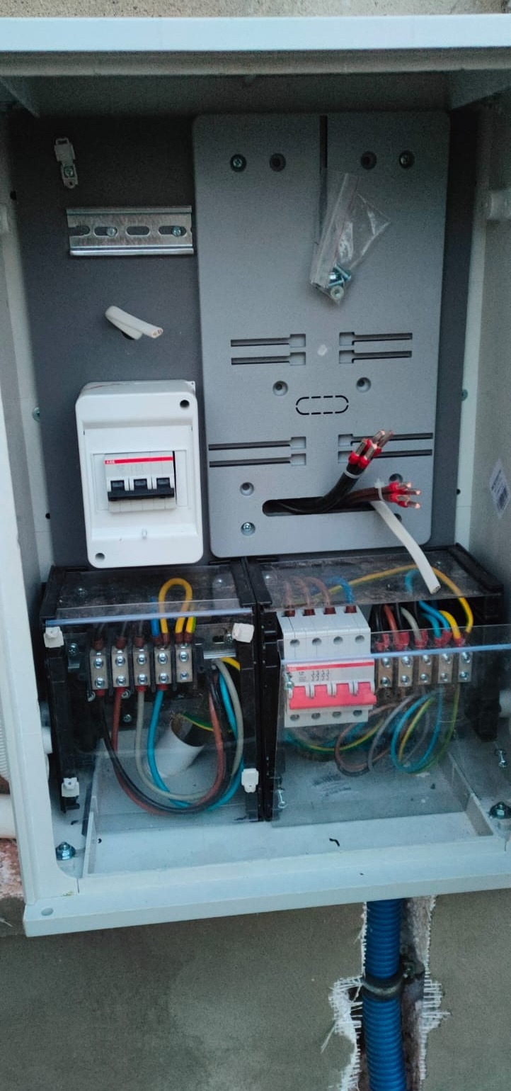 Wnętrze skrzynki elektrycznej z zainstalowanymi zabezpieczeniami, przewodami i elementami montażowymi. Widoczna instalacja elektryczna w budynku.