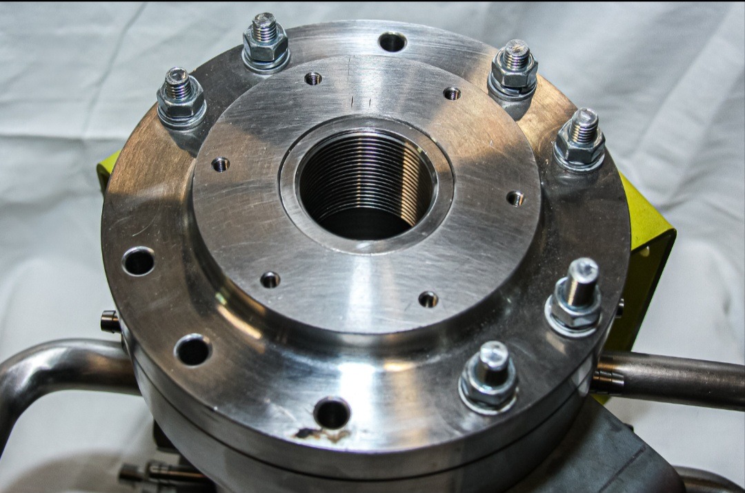 Metalowy element z gwintem wewnętrznym i śrubami, prawdopodobnie wykonany na tokarce, widoczny na tle białego materiału.