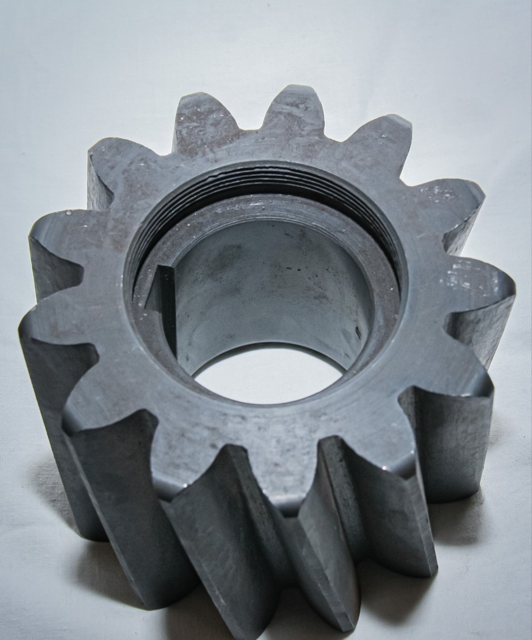 Metalowe koło zębate z wewnętrznym gwintem, wykonane metodą obróbki skrawaniem, leżące na białym tle. Widoczne ślady obróbki.