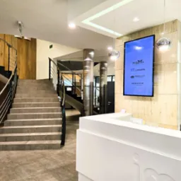 Recepcja w nowoczesnym biurze z marmurową ścianą, schodami i wiszącymi lampami. Na ścianie logo firm Pokorni, Copadata, Rebound i IdeaOffice.