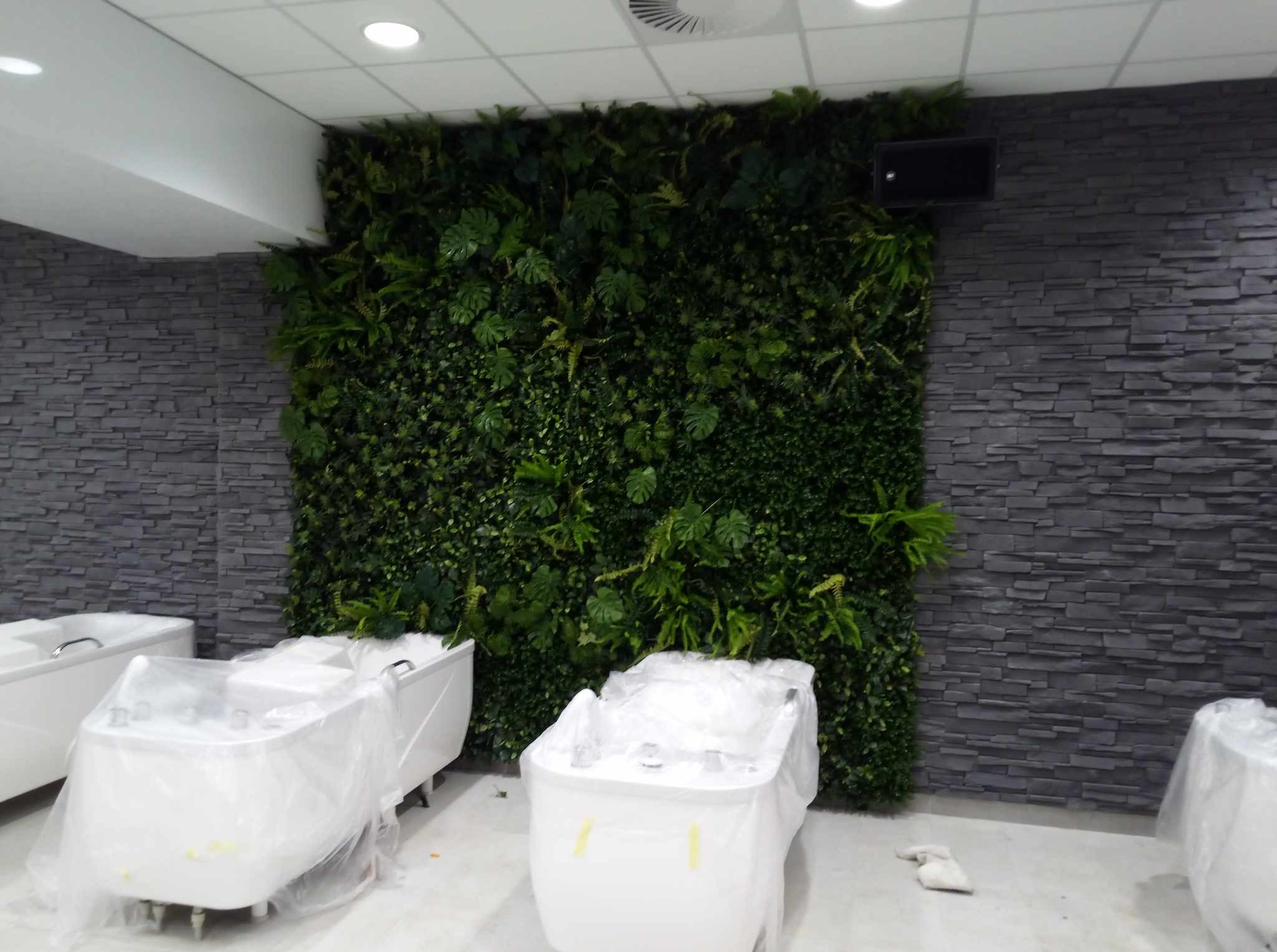 Ściana z kamienia i zieleni w łazience, z zakrytymi folią wannami z hydromasażem. Nowoczesny design, oświetlenie sufitowe. Wykończenie wnętrza.