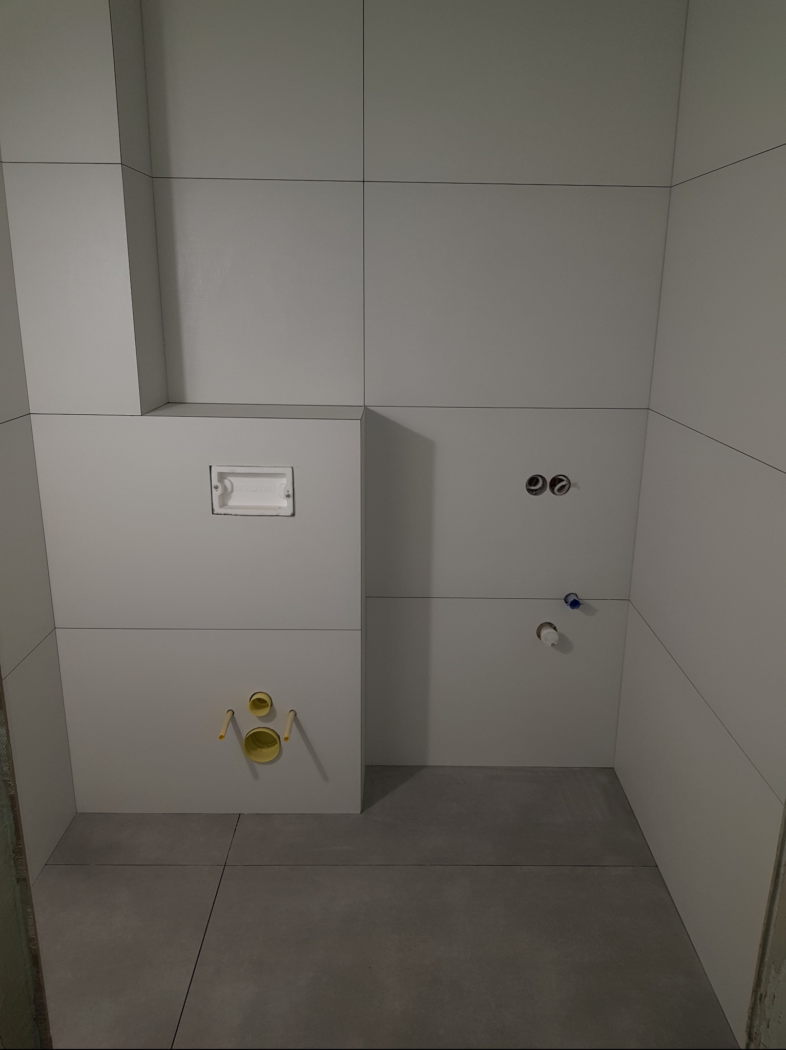 Wykończona łazienka w Warszawie z szarymi płytkami. Widoczne podejścia pod sanitariaty i stelaż podtynkowy WC. Minimalistyczny styl, jasne wnętrze, precyzyjne ułożenie płytek.