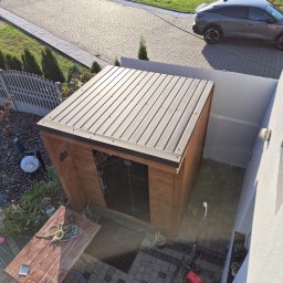 Radek Rybak - Nowoczesna, drewniana altana z metalowym dachem w ogrodzie, widziana z góry. Obok zaparkowany samochód i narzędzia ogrodowe na brukowanej powierzchni.