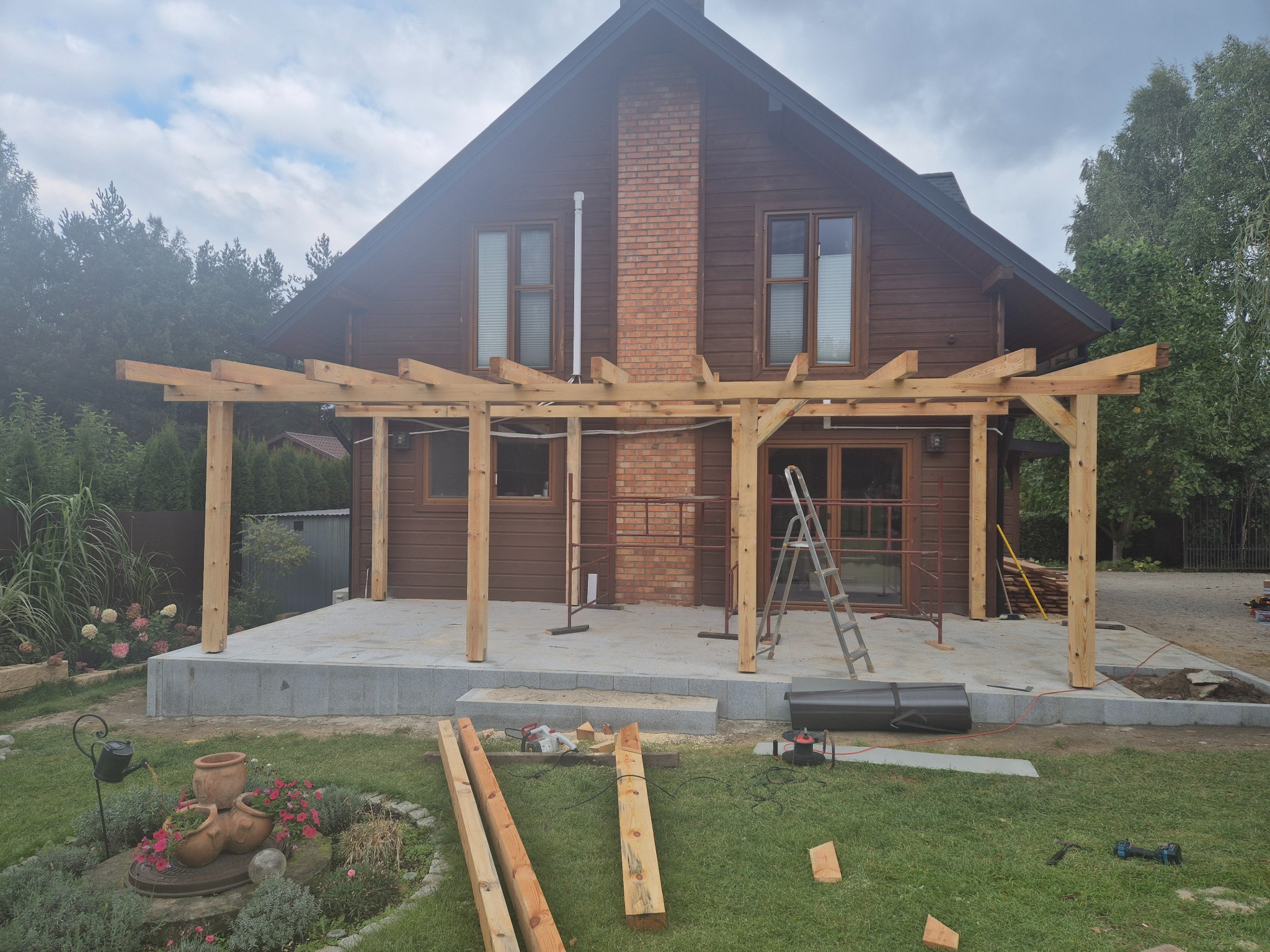 Drewniana konstrukcja pergoli w trakcie montażu przy domu w Piotrków Trybunalski. Widoczne narzędzia i elementy konstrukcyjne na trawniku.