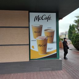 BAD BOYS AGENCY SPÓŁKA Z OGRANICZONĄ ODPOWIEDZIALNOŚCIĄ - Reklama McCafé na zewnątrz budynku z kobietą w czarnym płaszczu. Plakat prezentuje cappuccino, flat white i caramel latte macchiato.