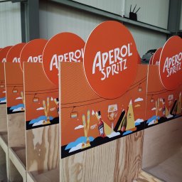 BAD BOYS AGENCY SPÓŁKA Z OGRANICZONĄ ODPOWIEDZIALNOŚCIĄ - Rząd ekspozytorów Aperol Spritz z motywem zimowym, widoczne logo i grafika, wykonane w Warszawie. Konstrukcja z surowego drewna, pomarańczowe elementy.