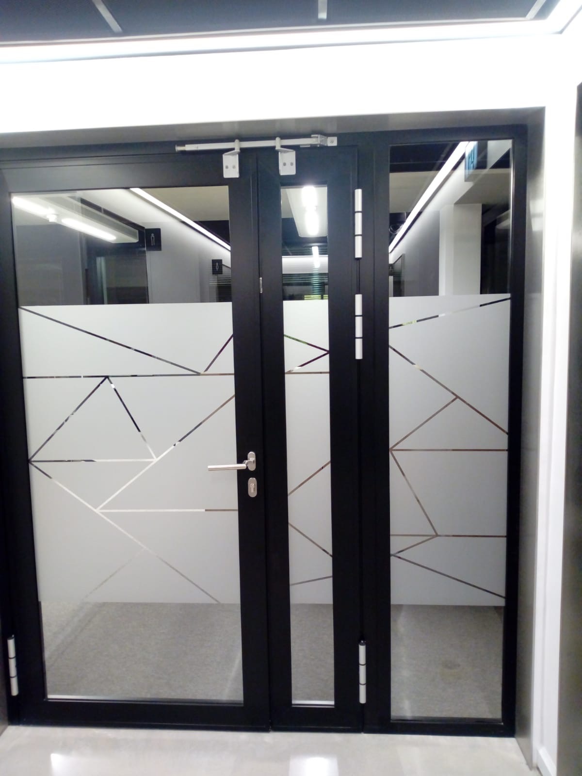 Czarne drzwi biurowe z matową folią w geometryczne wzory, widoczne wnętrze z oświetleniem LED. Minimalistyczny design, nowoczesne wykończenie.
