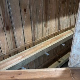 Expo-Activ - Drewniany strop z widocznymi belkami i elementami mocującymi, prawdopodobnie przygotowany pod montaż sufitu napinanego. Widok z dołu, surowe drewno.